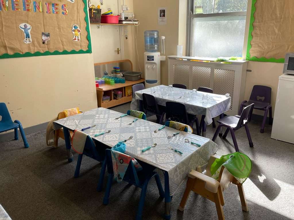 Dining tables set for snack time next to a water station in a nursery room at Ducklings Nursery, Moldgreen