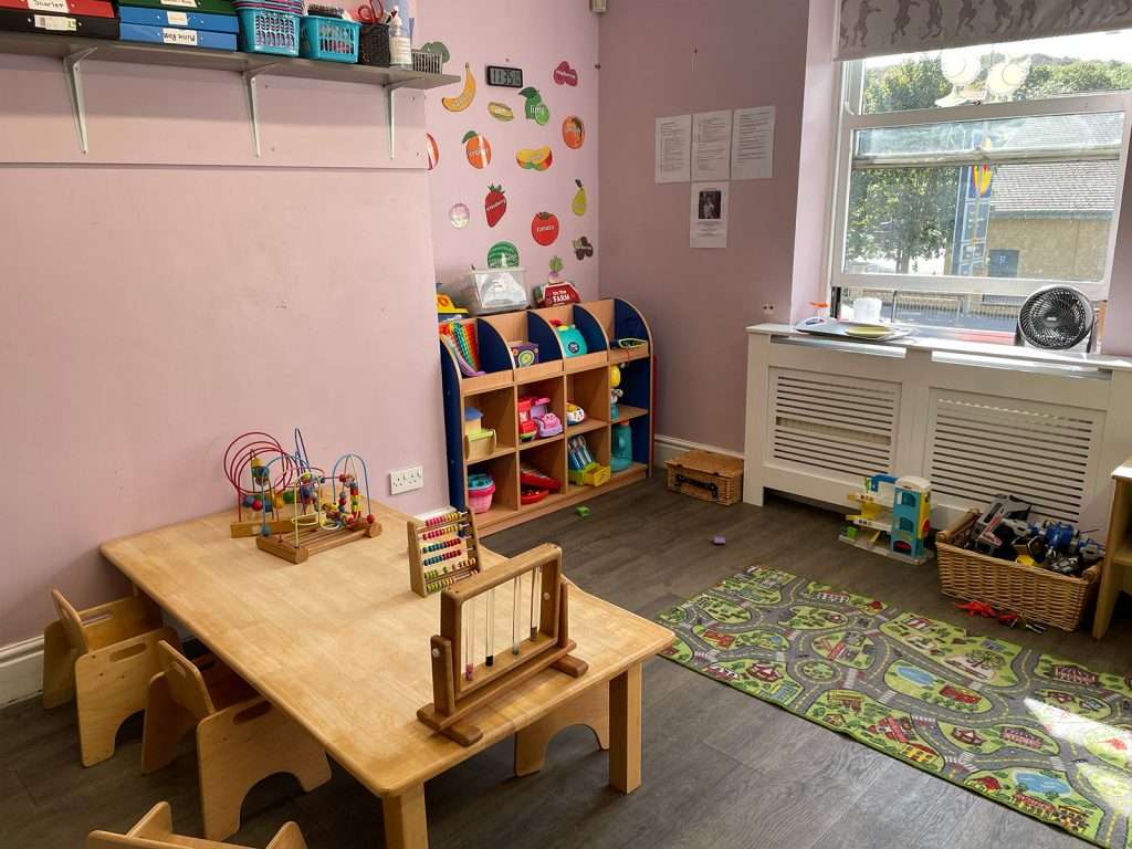 Wooden activity table with toys and colourful storage shelving in a bright playroom at Ducklings Childcare nursery, Huddersfield